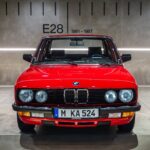 BMW roșu fotografiat frontal în fața panoului E28, 1981-1987, la BMW Museum München.