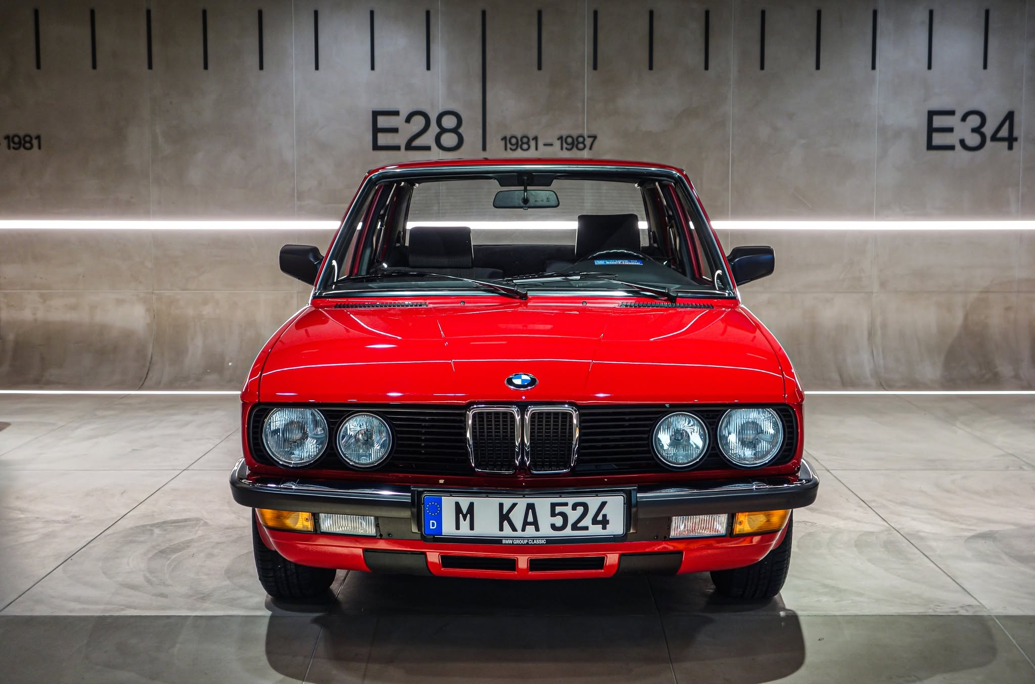 BMW roșu fotografiat frontal în fața panoului E28, 1981-1987, la BMW Museum München.