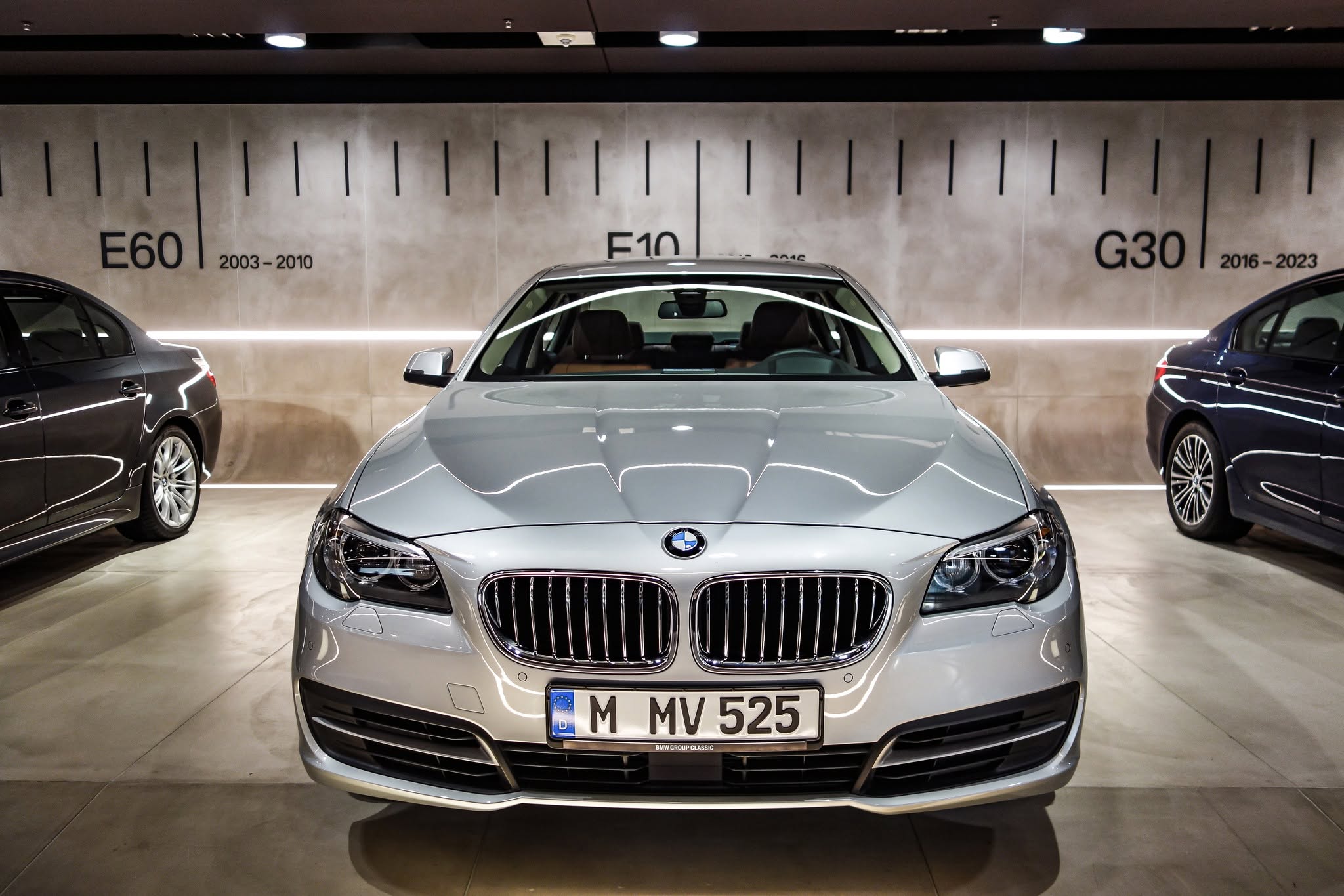 Automobil BMW argintiu văzut din față, cu panoul generațiilor E60, F10 și G30 în fundal, la BMW Museum München.