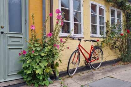 Bicicletă roșie lângă o fațadă galbenă, ușă verde și flori în Copenhaga
